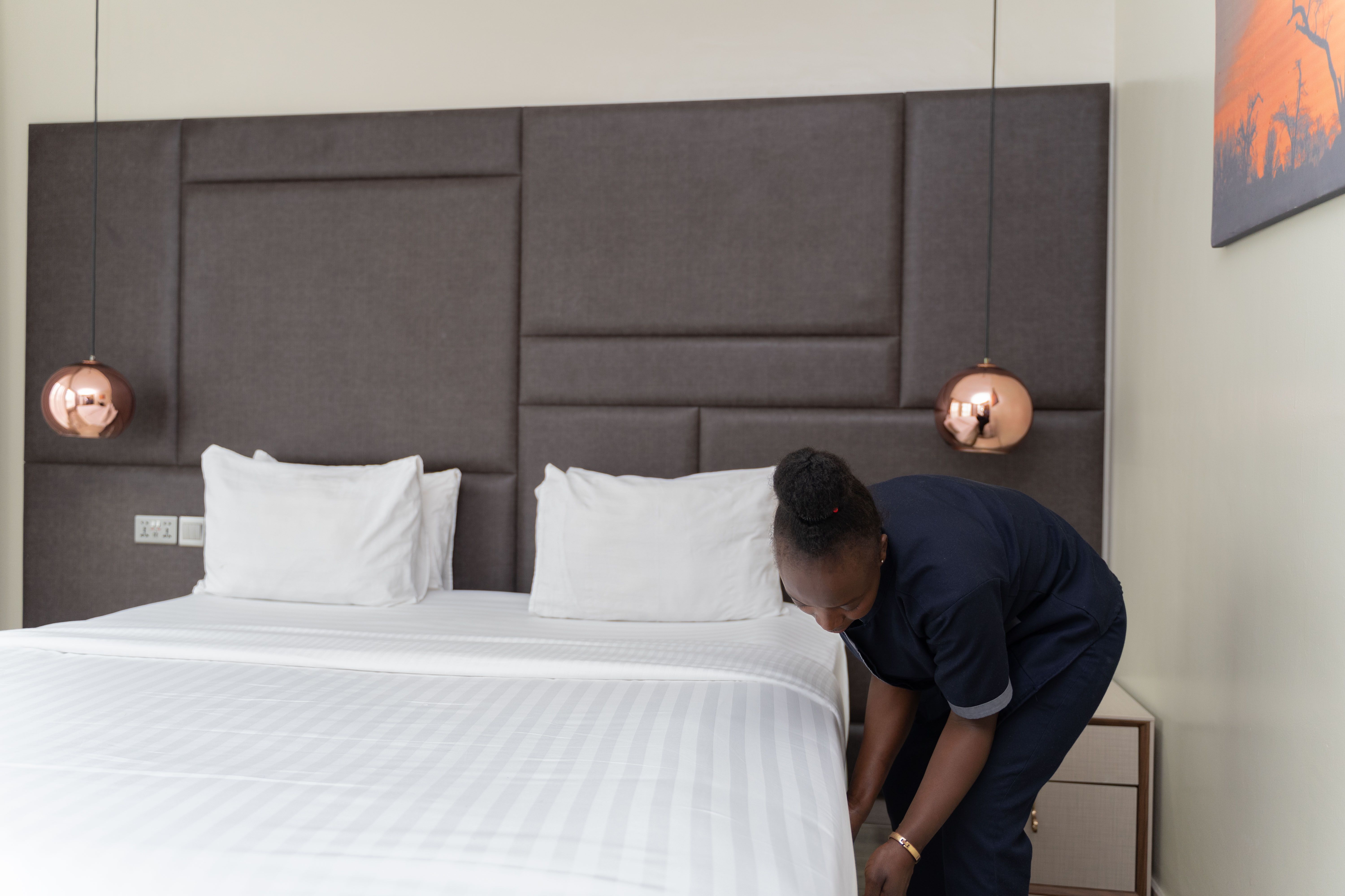 A cleaner preparing a bed with fresh linen in a modern room during a turnover clean.