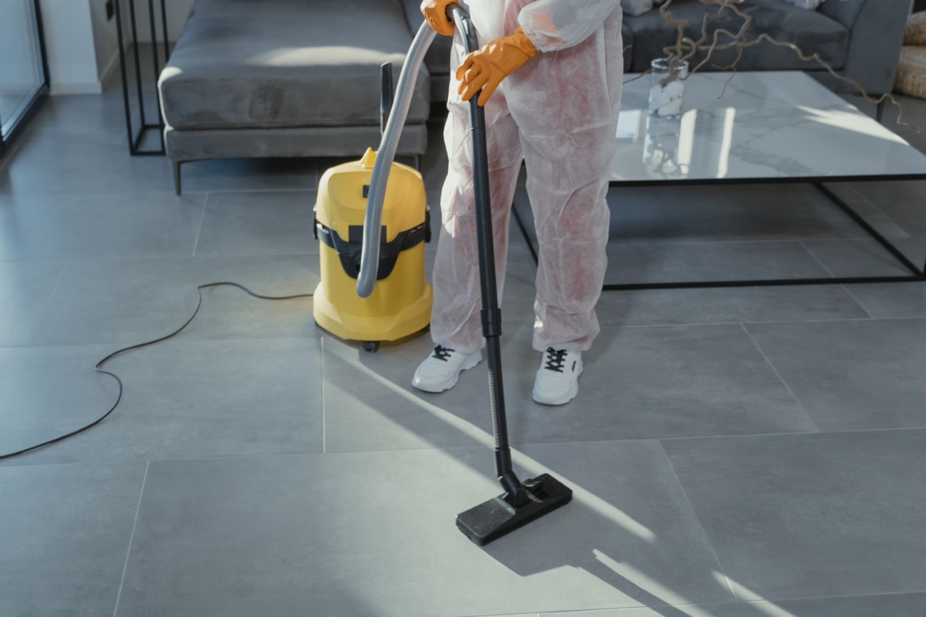 A professional cleaner in protective gear vacuuming a modern living room floor
