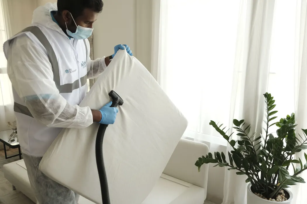 A cleaner in protective gear vacuuming a mattress during a deep clean.