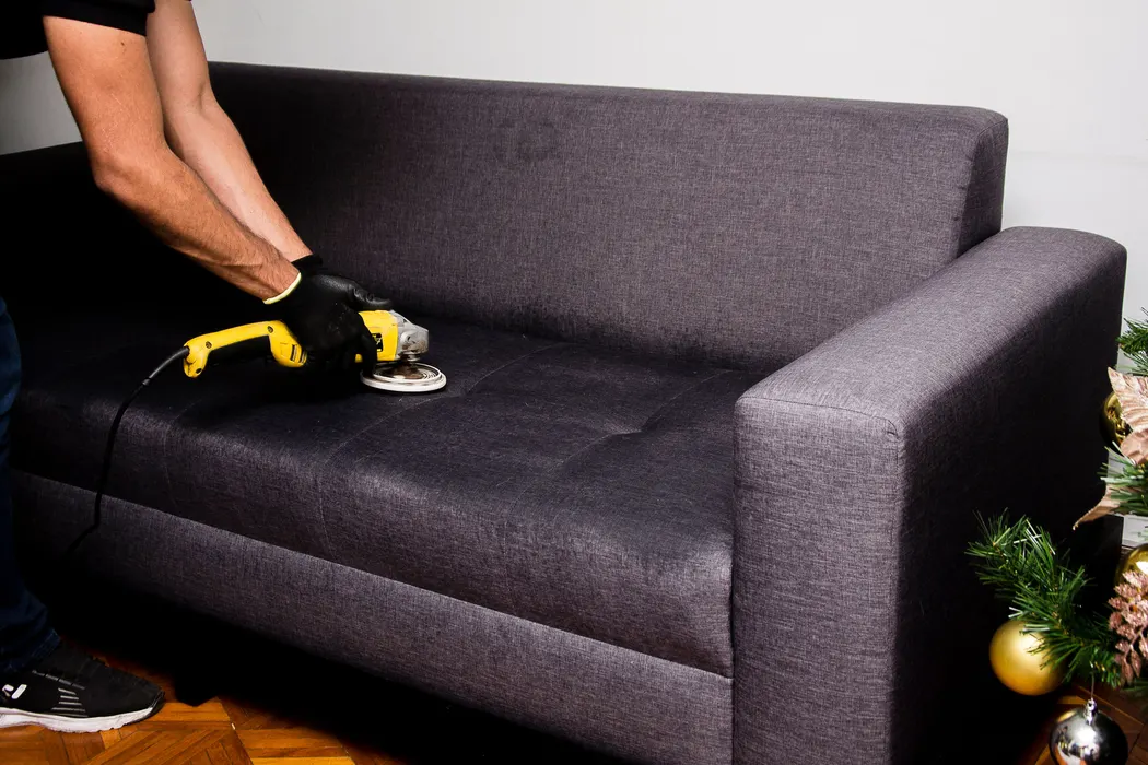 A professional cleaning technician deep-cleaning a sofa with equipment.