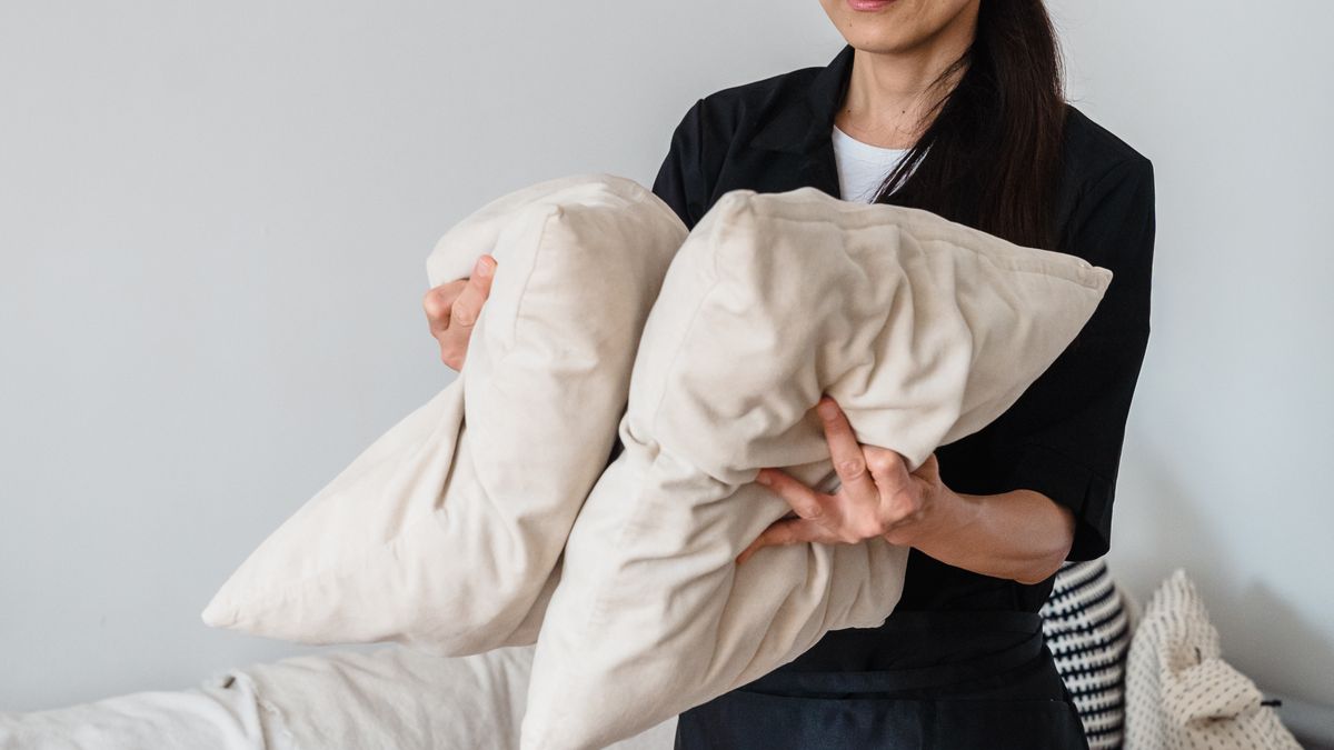 Smiling housekeeper arranging pillows on a sofa in a bright living room