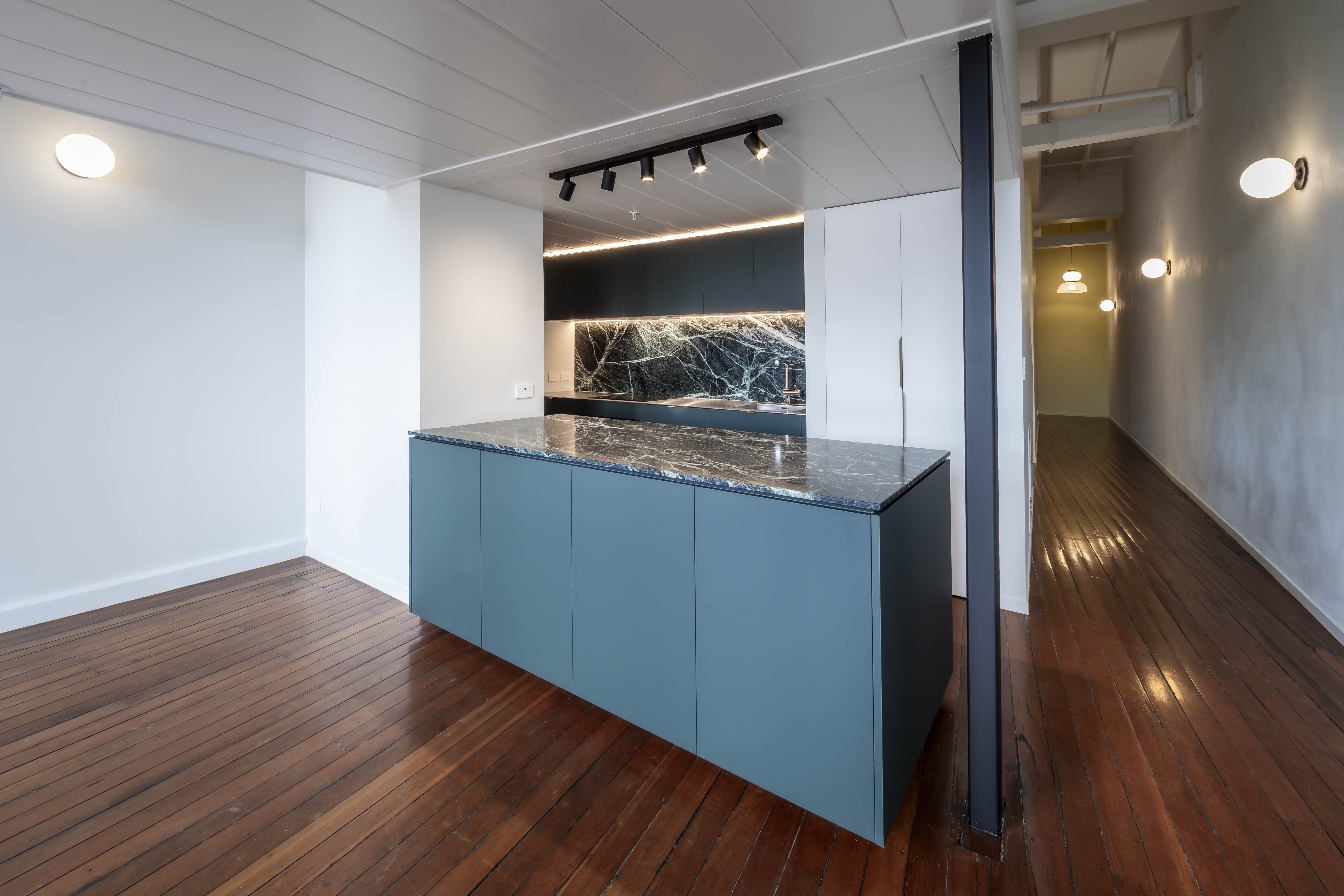 Custom kitchen cabinetry, dark natural stone and teal island at George Court Apartment in Auckland