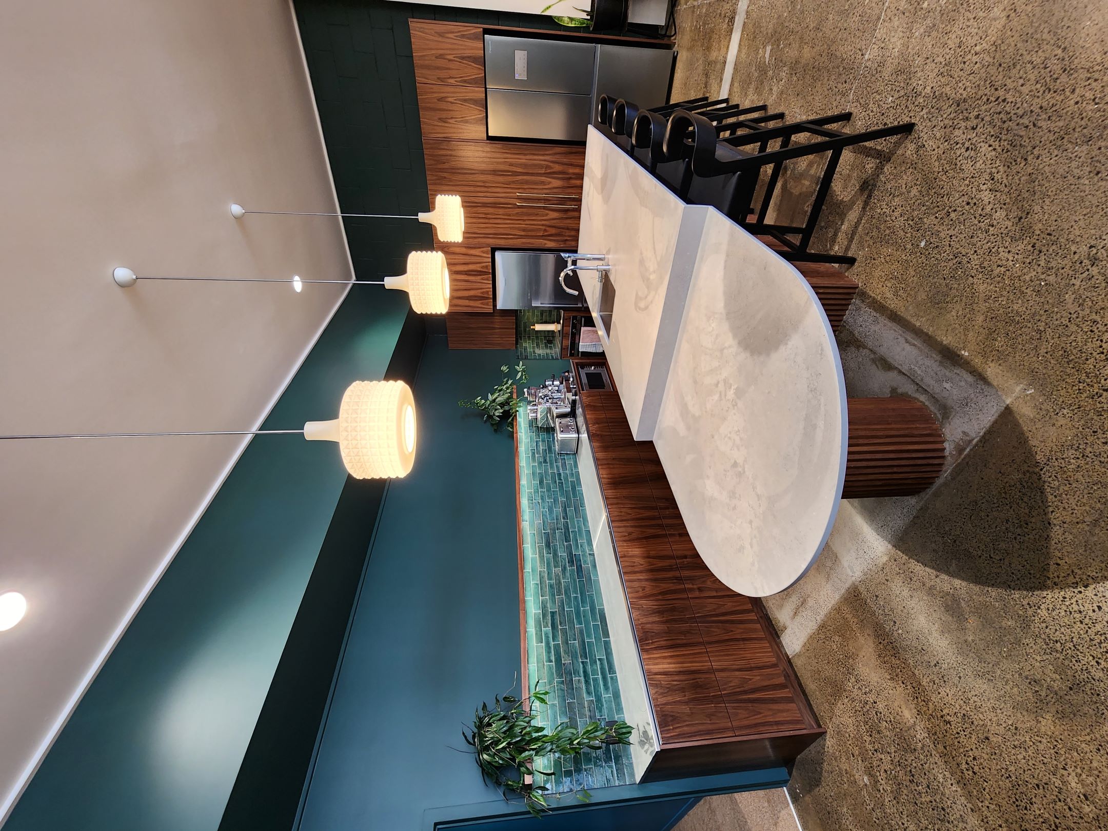Finch Office breakout kitchen with curved stone-topped island, ribbed timber-grain base and green cabinetry