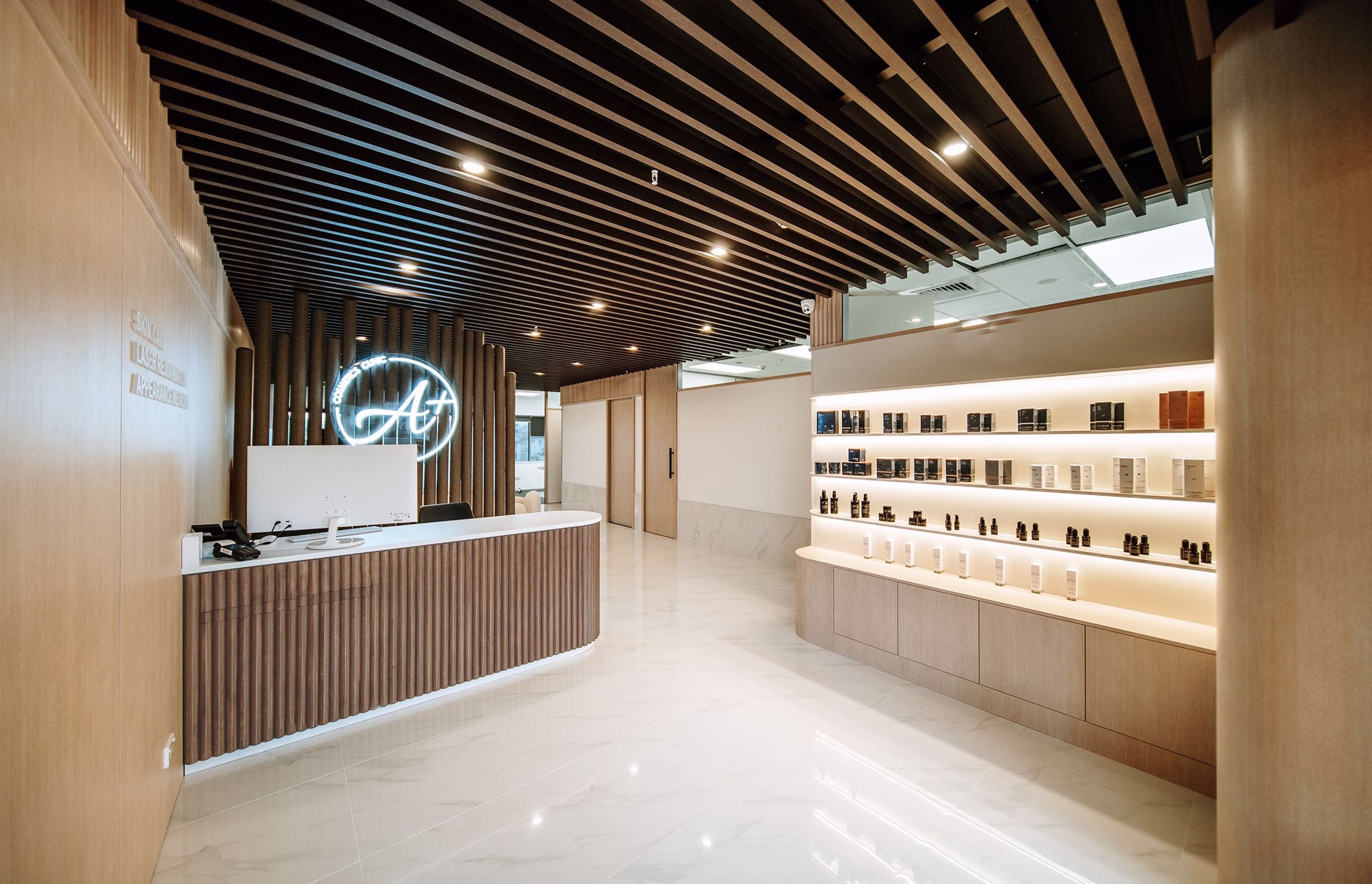 A+ Cosmetic Clinic reception with curved counter, illuminated product-display cabinetry, timber wall panelling and dark slatted feature ceiling