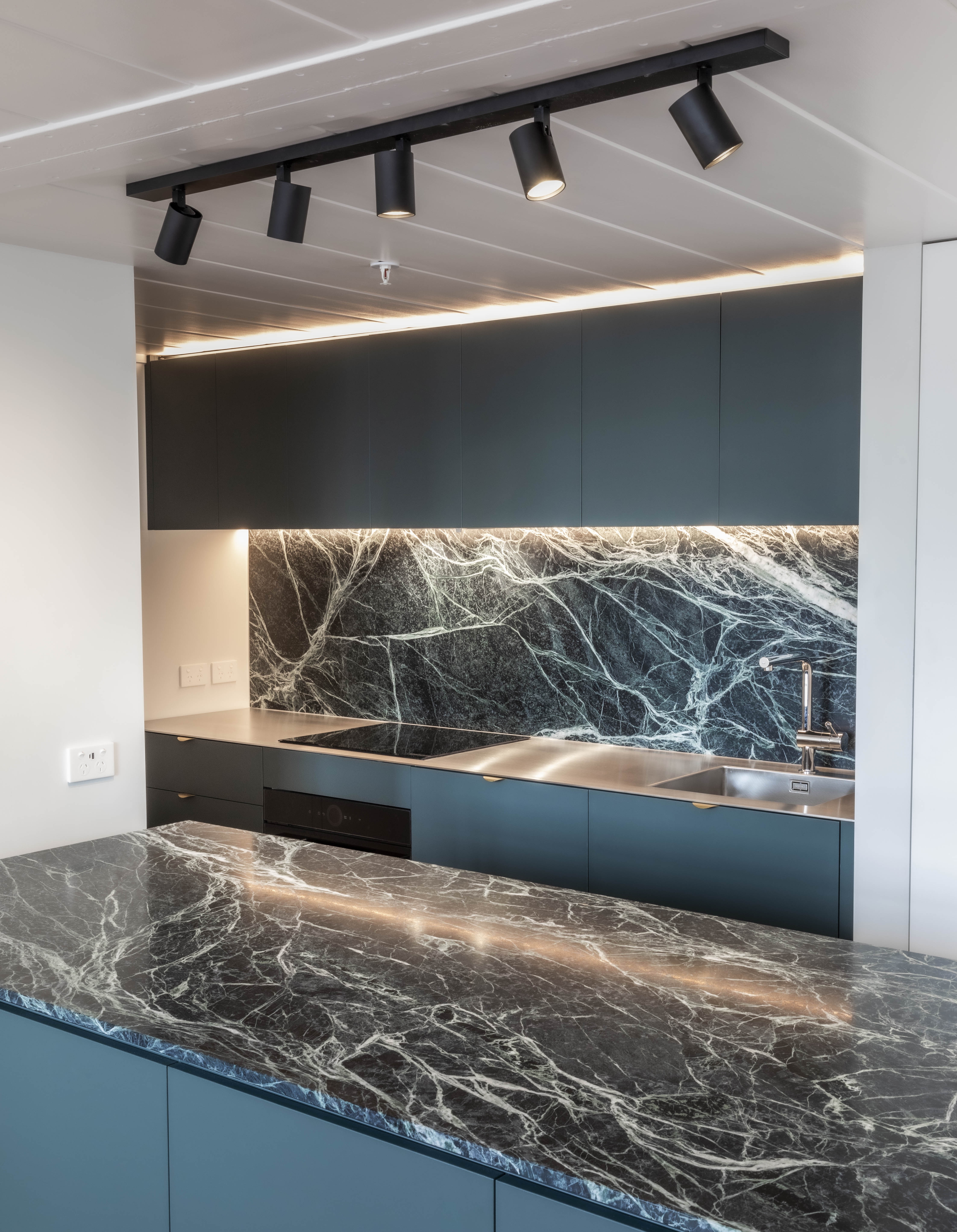 Custom kitchen cabinetry with teal island, dark stone and integrated lighting at George Court Apartment