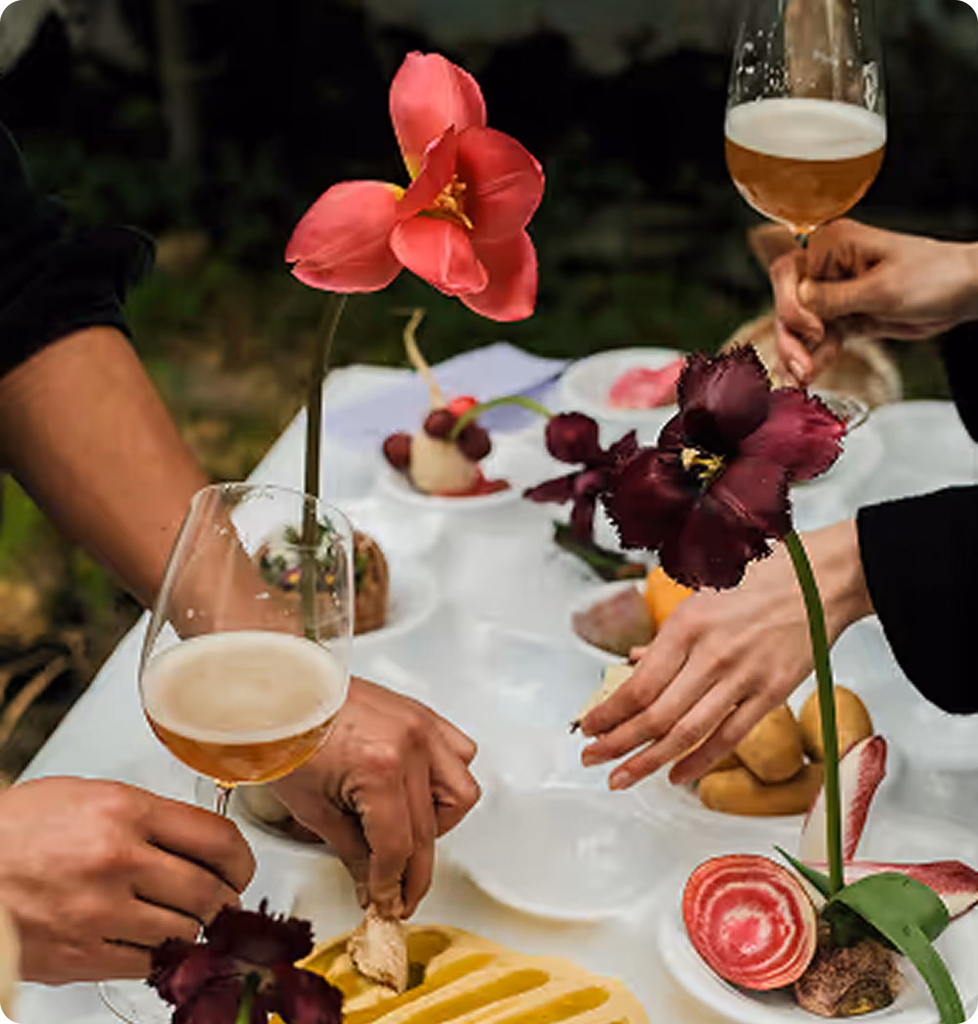 Deux mains tenant des verres de bière près d'une table avec des fleurs et des amuse-bouches.