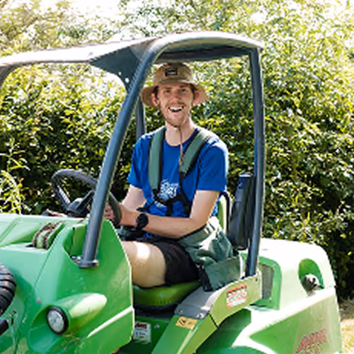 Homme souriant portant un chapeau assis dans un véhicule utilitaire vert à l'extérieur.