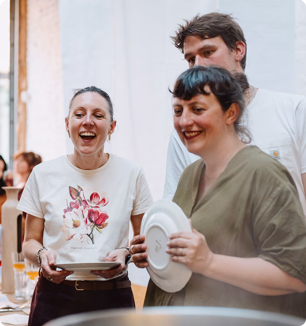 Trois personnes souriantes discutent en tenant des assiettes dans une ambiance chaleureuse.