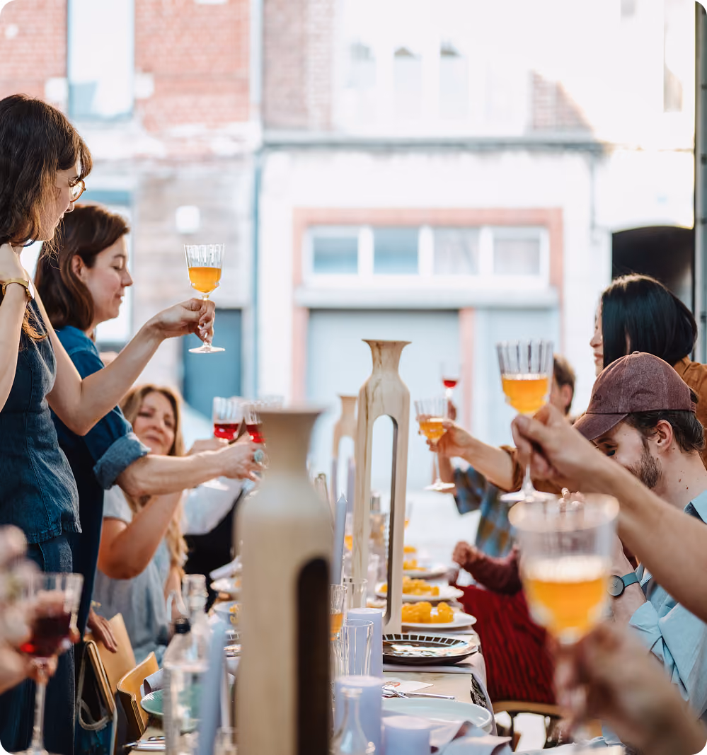 Des personnes assises à une longue table, levant leurs verres pour un toast lors d'un repas convivial.
