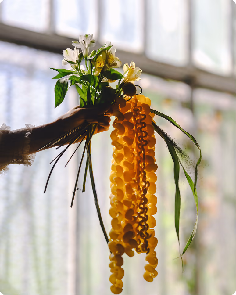 Une main tenant un bouquet de fleurs blanches et une longue guirlande jaune translucide.