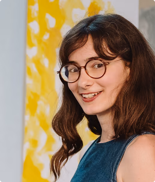Jeune femme souriante aux cheveux longs et lunettes rondes, devant un fond jaune abstrait.