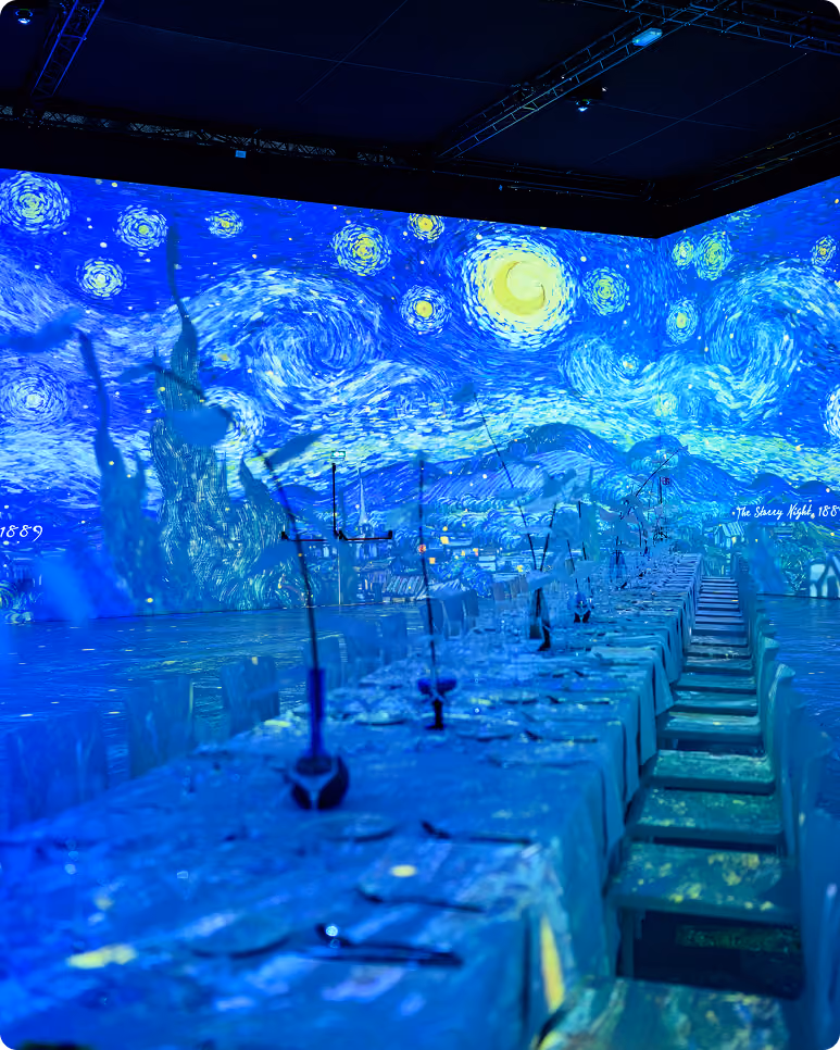 Salle avec une longue table dressée et une projection immersive de La Nuit étoilée de Van Gogh.