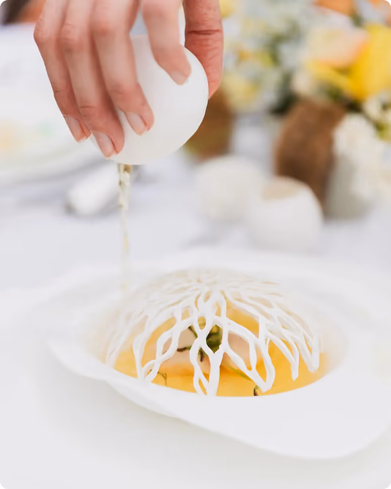 Une main casse un œuf sur un plat orné d'une structure comestible décorative blanche.