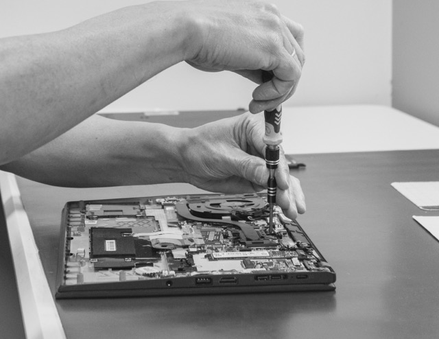 Technician using a screwdriver to repair an opened laptop.