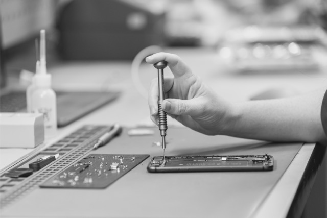 Technician using a precision screwdriver to repair an opened smartphone.