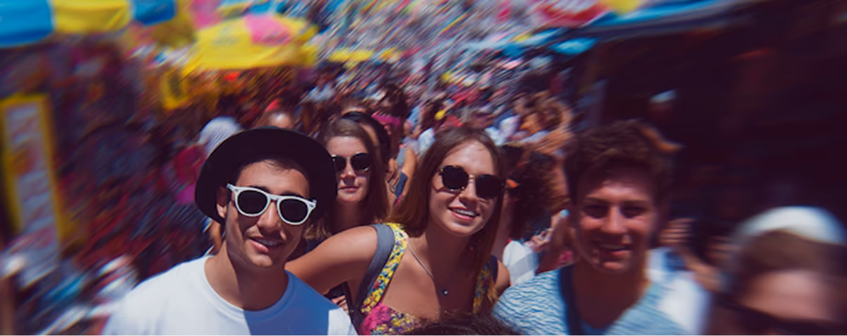 Group of young adults wearing sunglasses smiling in a crowded outdoor festival.