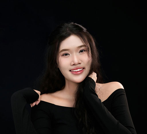 Smiling young woman with long dark hair wearing a black off-shoulder top against black background.