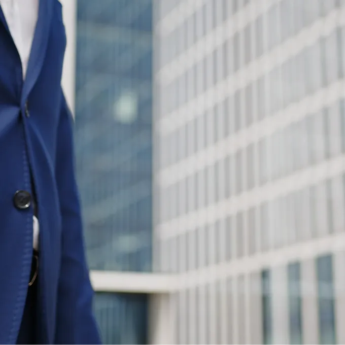 Person in blue suit standing in front of a modern glass office building.