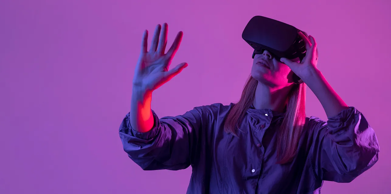 Woman with long hair using a VR headset reaching out with her hand against a purple background.