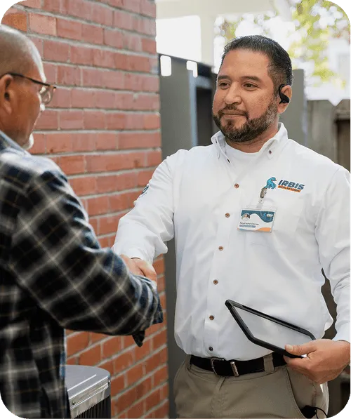 Technician in white shirt shaking hands with an older man in a plaid shirt outside near a brick wall, holding a tablet.