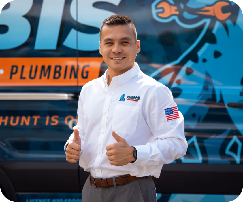 Smiling man in a white Irbis Plumbing shirt with an American flag patch giving two thumbs up in front of a branded service van.