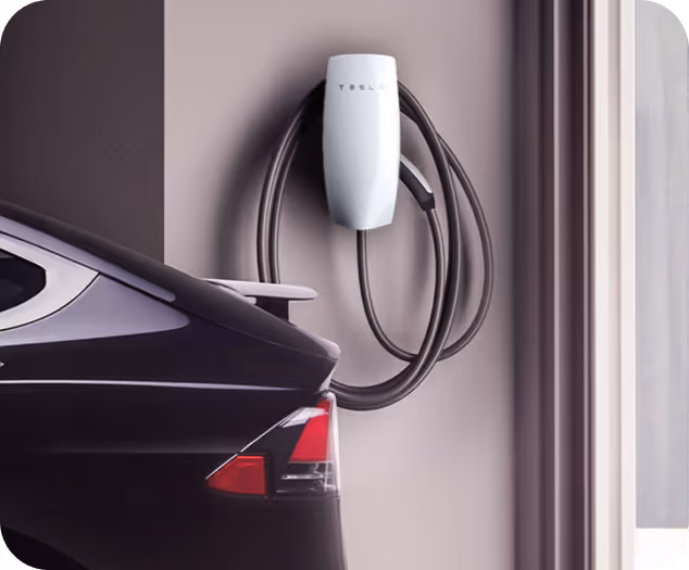 Black Tesla electric car parked near a white Tesla wall-mounted charger with coiled cable.