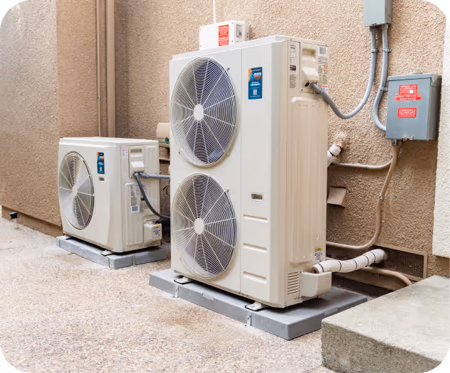 Two outdoor air conditioning units installed on concrete pads next to a building wall.