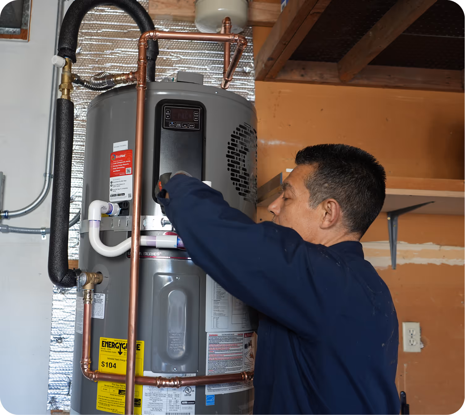 Technician adjusting controls on a gray water heater tank with copper and insulated pipes in a basement.