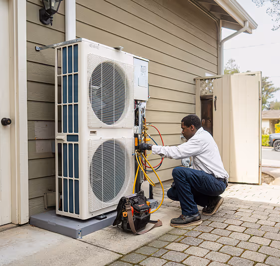 Technician kneeling and repairing outdoor air conditioning unit next to house wall.