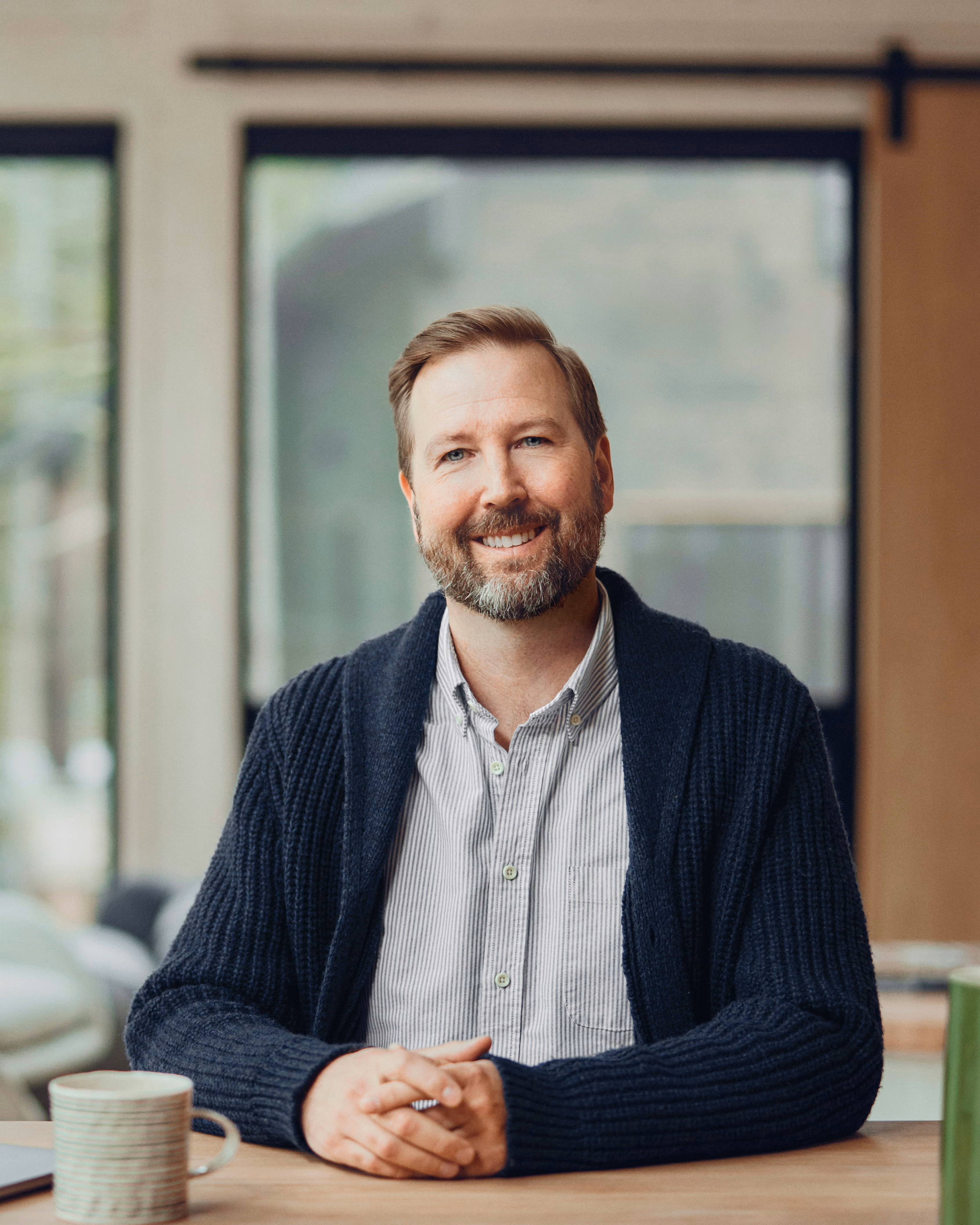 David Pio, co-founder and COO of Birch Point Wealth Management, smiling at a wooden table in a bright, window-lit room