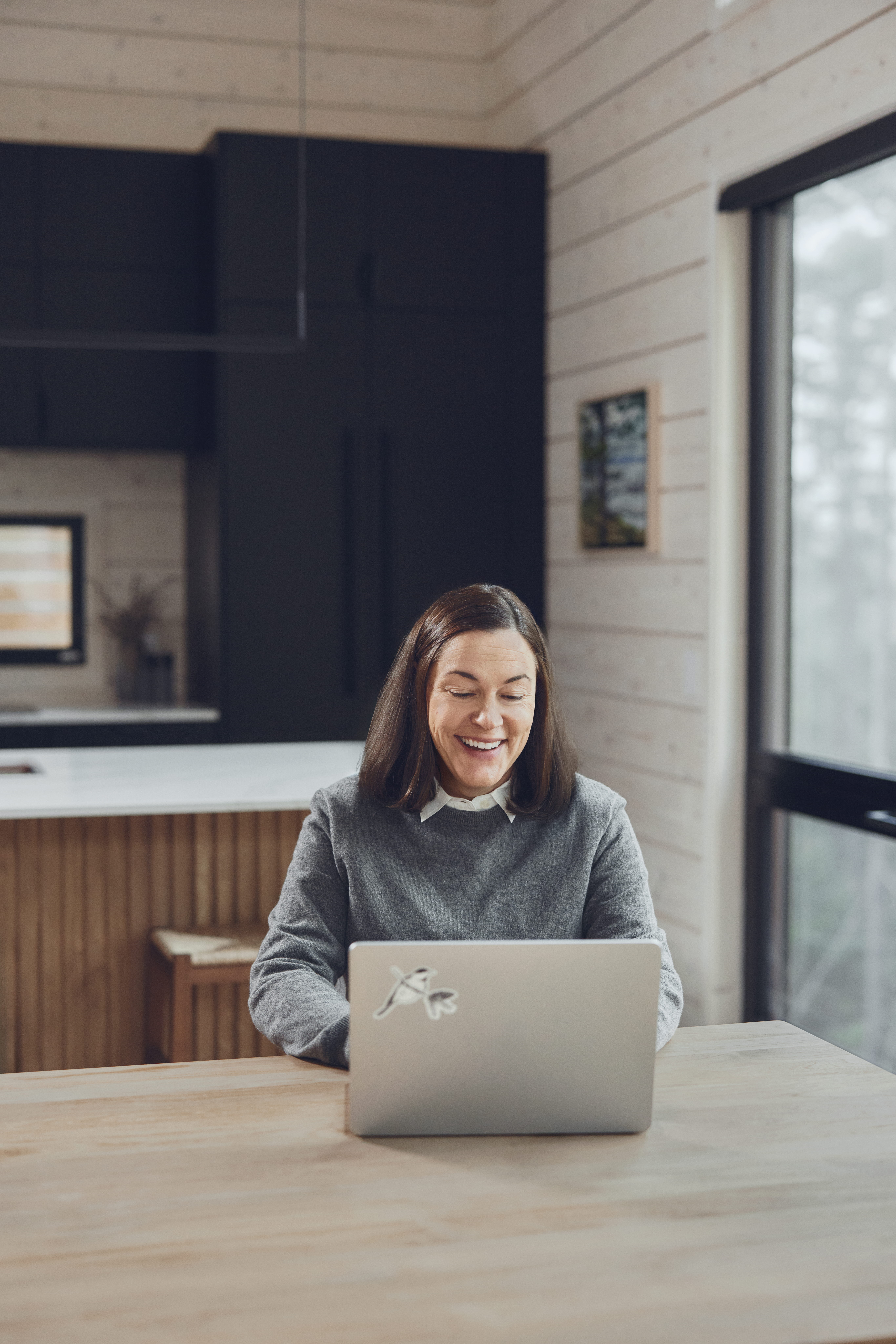 Brie Pio working on a laptop at a wooden table in a bright, wood-paneled room