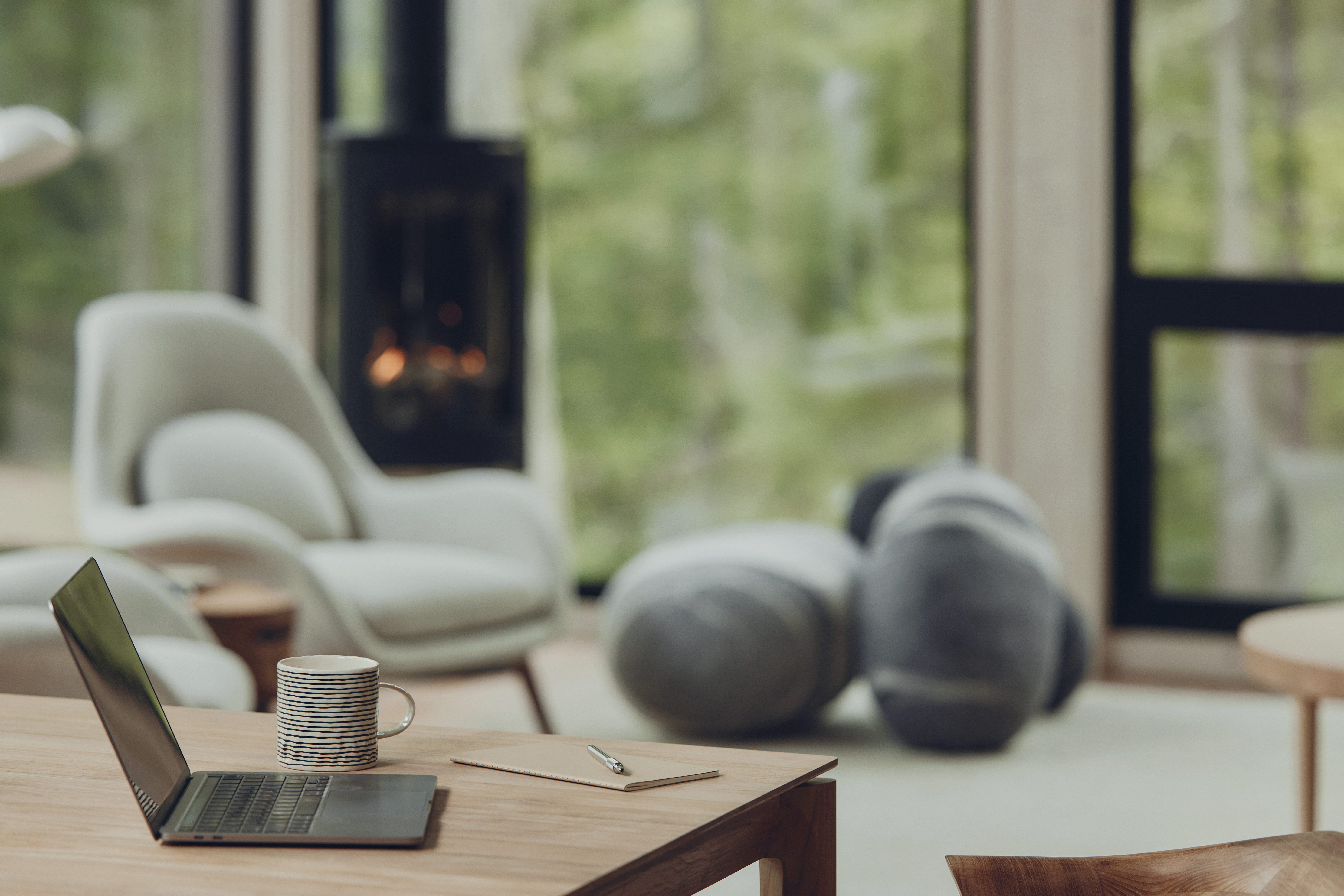 A quiet sitting area with lounge chairs and a wood stove beyond a wooden table