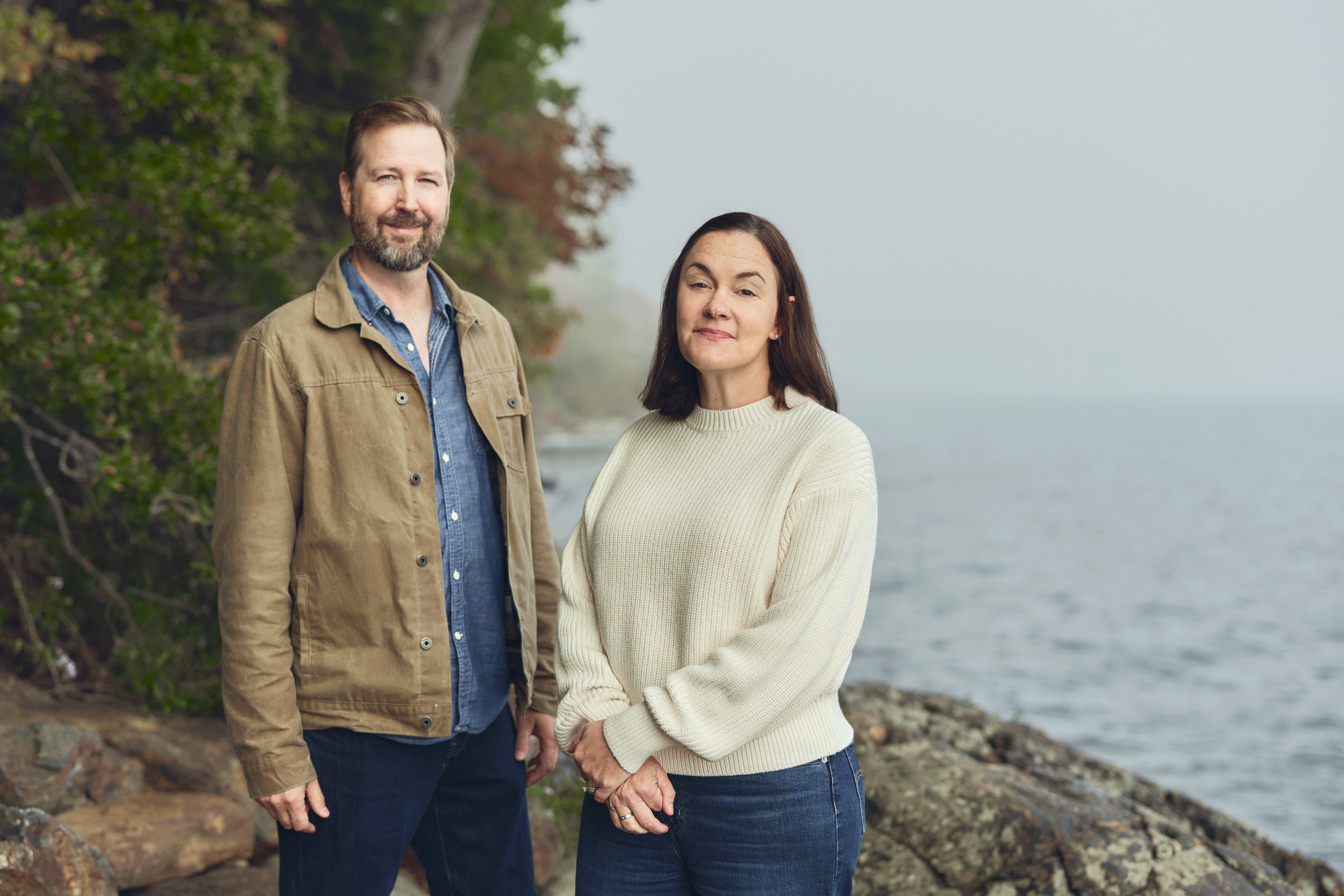 Brie and David Pio, founders of Birch Point Wealth Management, standing together on the foggy shore of Penobscot Bay in Camden Hills State Park