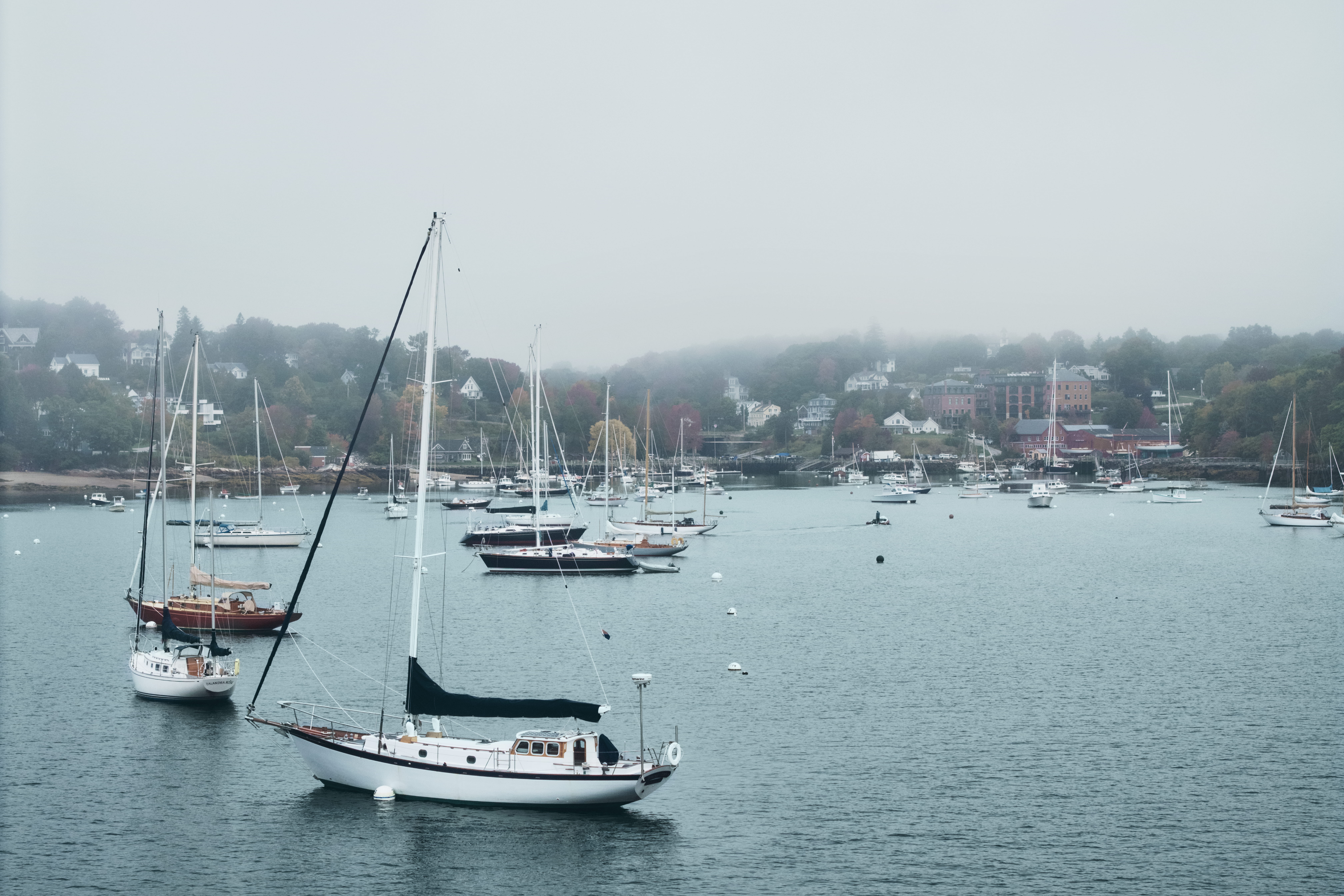 Sailboats moored in Rockport Harbor, Maine, with the village along the shore in the mist