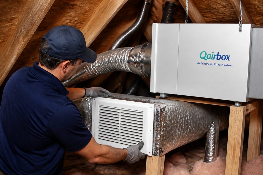 Professional HVAC technician installing return air grille in attic space, connecting ductwork to whole-home air purification system with visible sealing and connection points