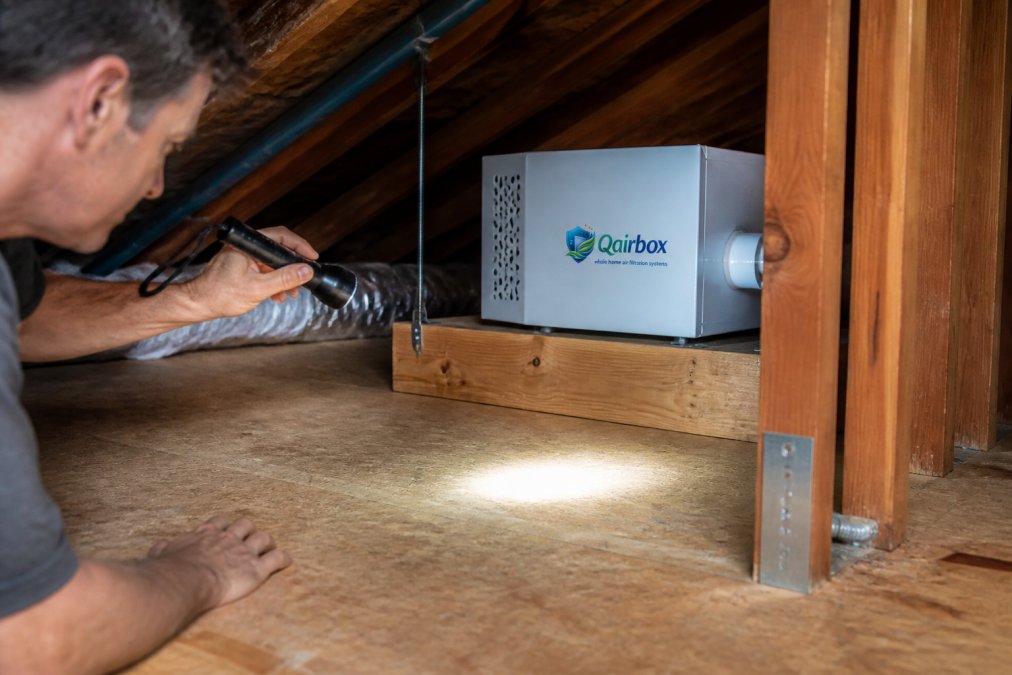 A homeowner's hand holding a flashlight, inspecting a clean and dry attic area near a professionally installed standalone air purification unit, highlighting a dust-free surface