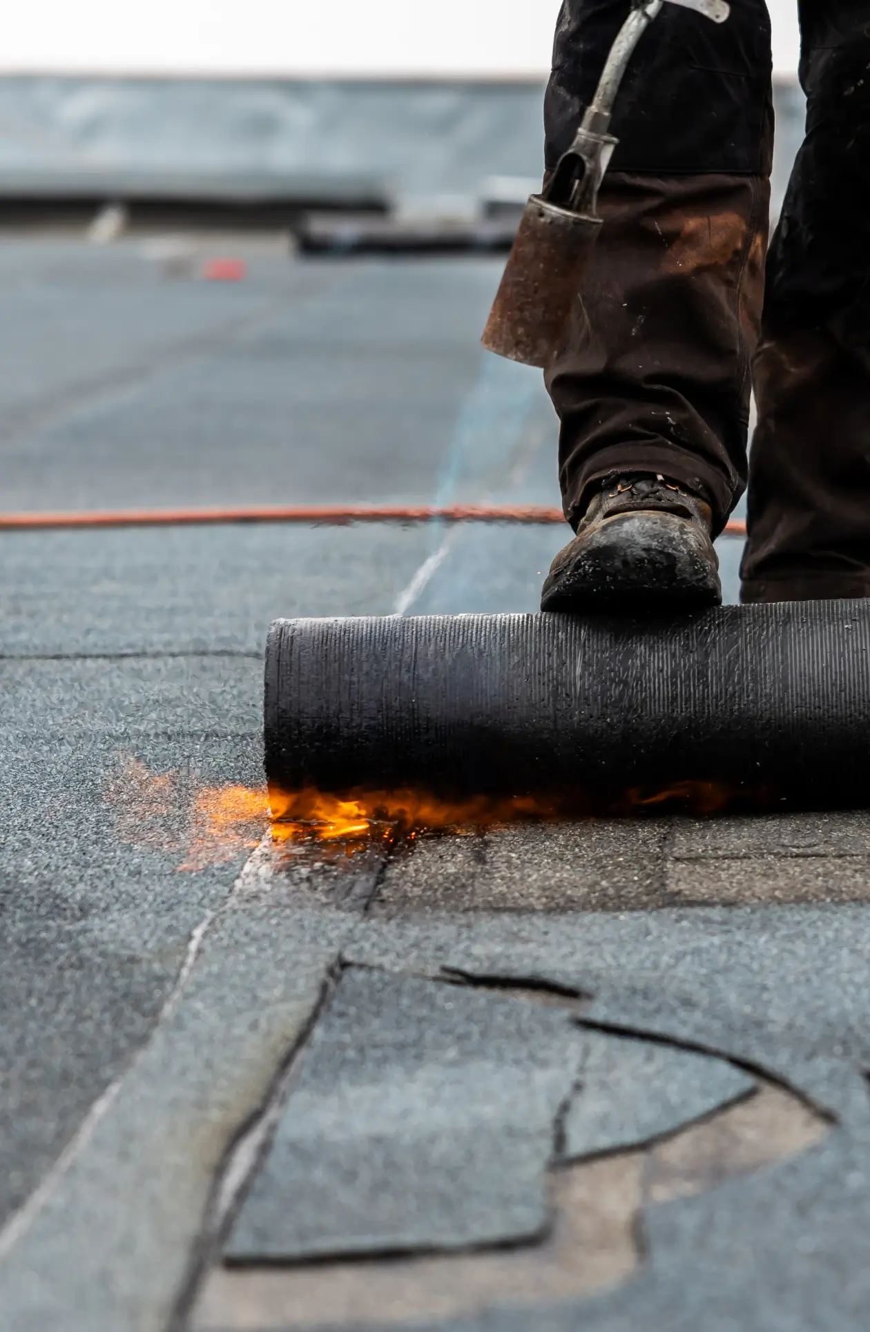 Worker applying heated bitumen roofing membrane with torch, sealing waterproof layer for durable flat‑roof protection.