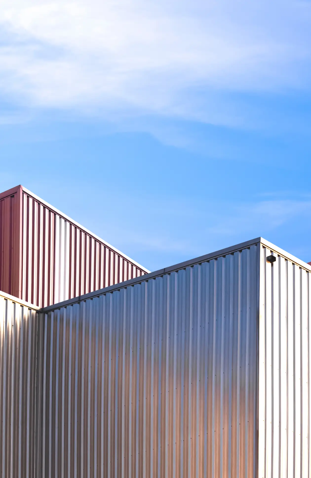 Modern industrial building with red and silver corrugated metal cladding under a clear blue sky, showcasing durable architectural design.
