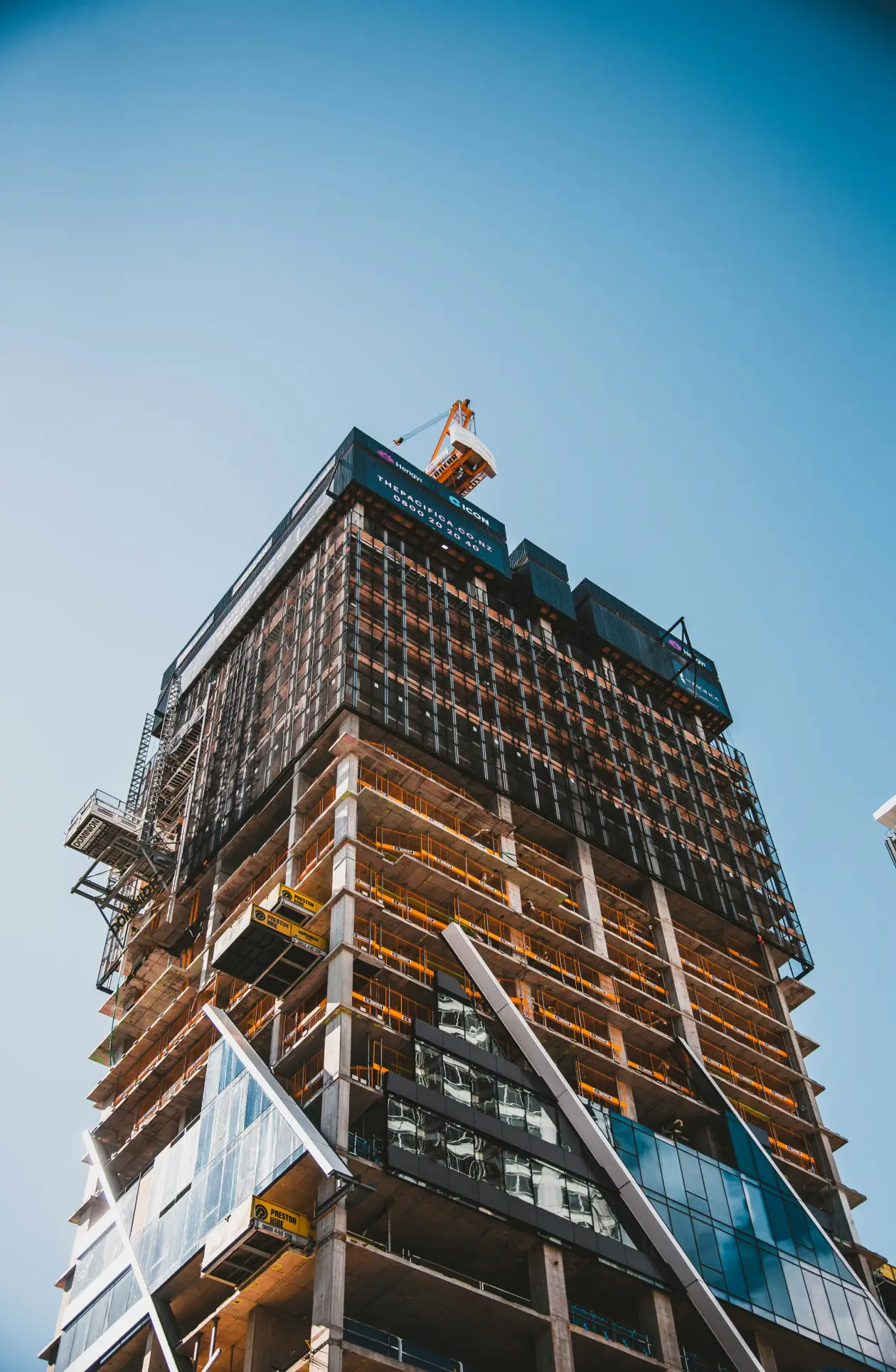 High‑rise building under construction with scaffolding, glass panels, and crane above, symbolizing precision and progress in commercial roofing projects.