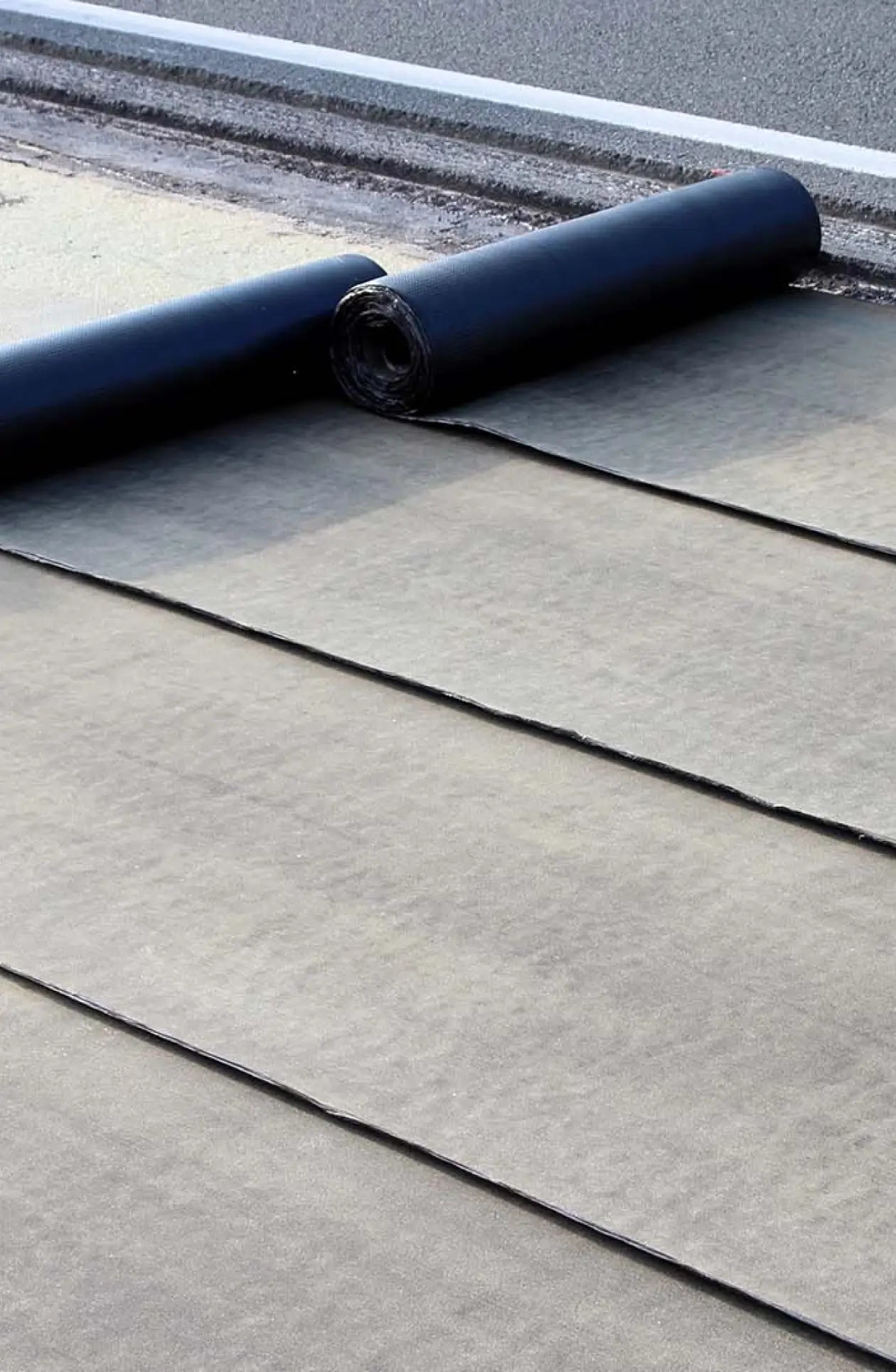 Close‑up of waterproof roofing membrane being unrolled in overlapping layers, illustrating precision and durability in roof replacement preparation.