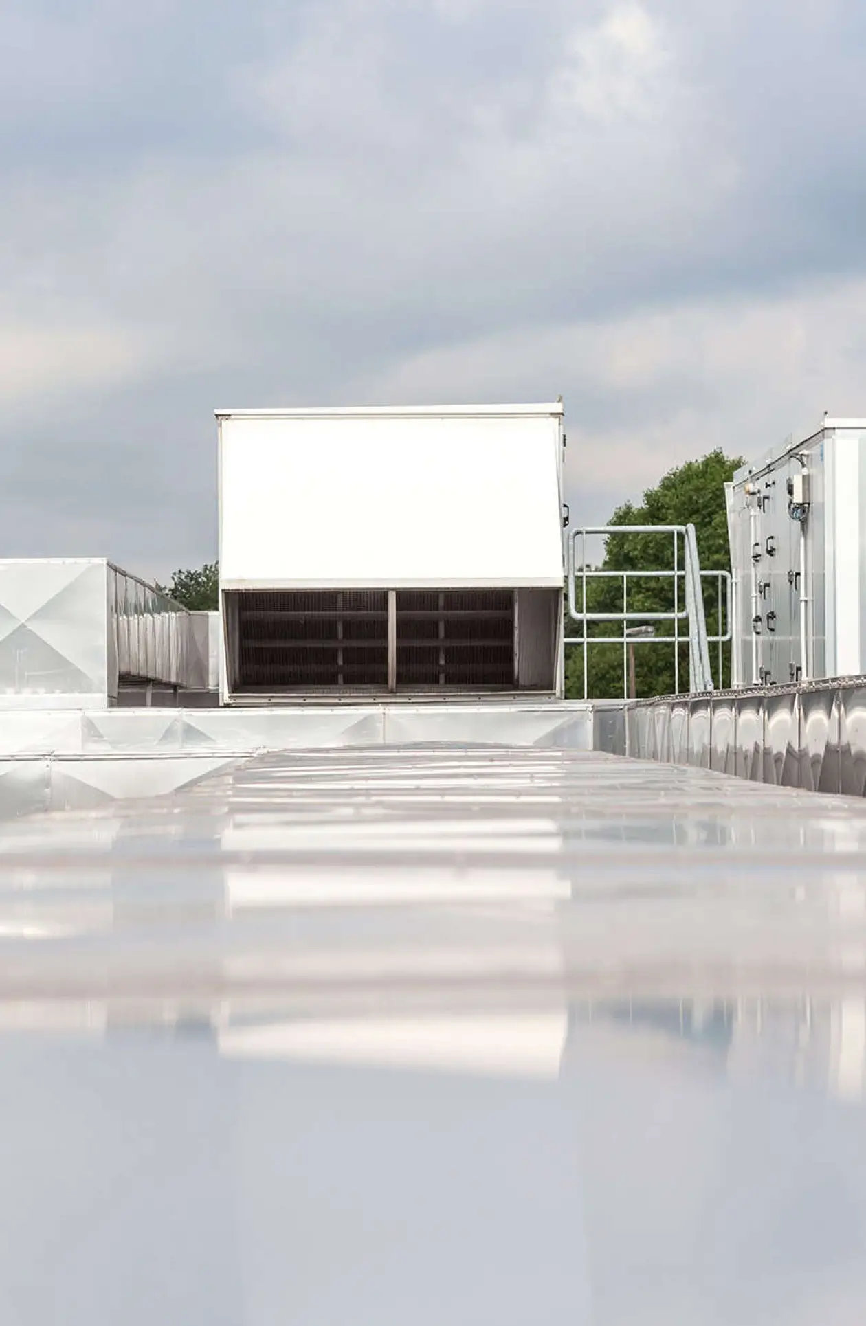 Flat commercial rooftop with white reflective membrane and HVAC units under cloudy sky, representing proactive maintenance for long‑term roof performance.