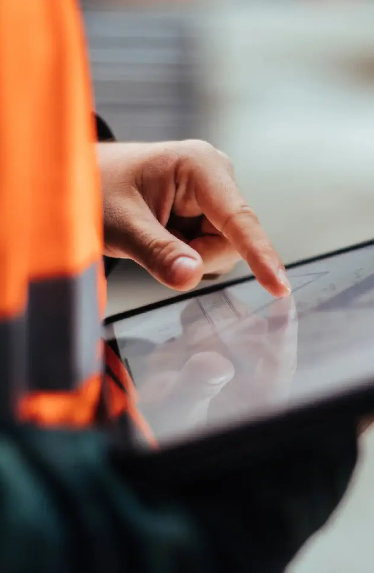 Close‑up of a construction professional in an orange safety vest using a tablet to review technical drawings, symbolizing precision and digital coordination.