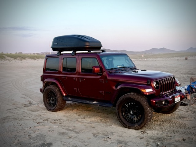 Red Jeep with a roof box parked on the beach at dusk