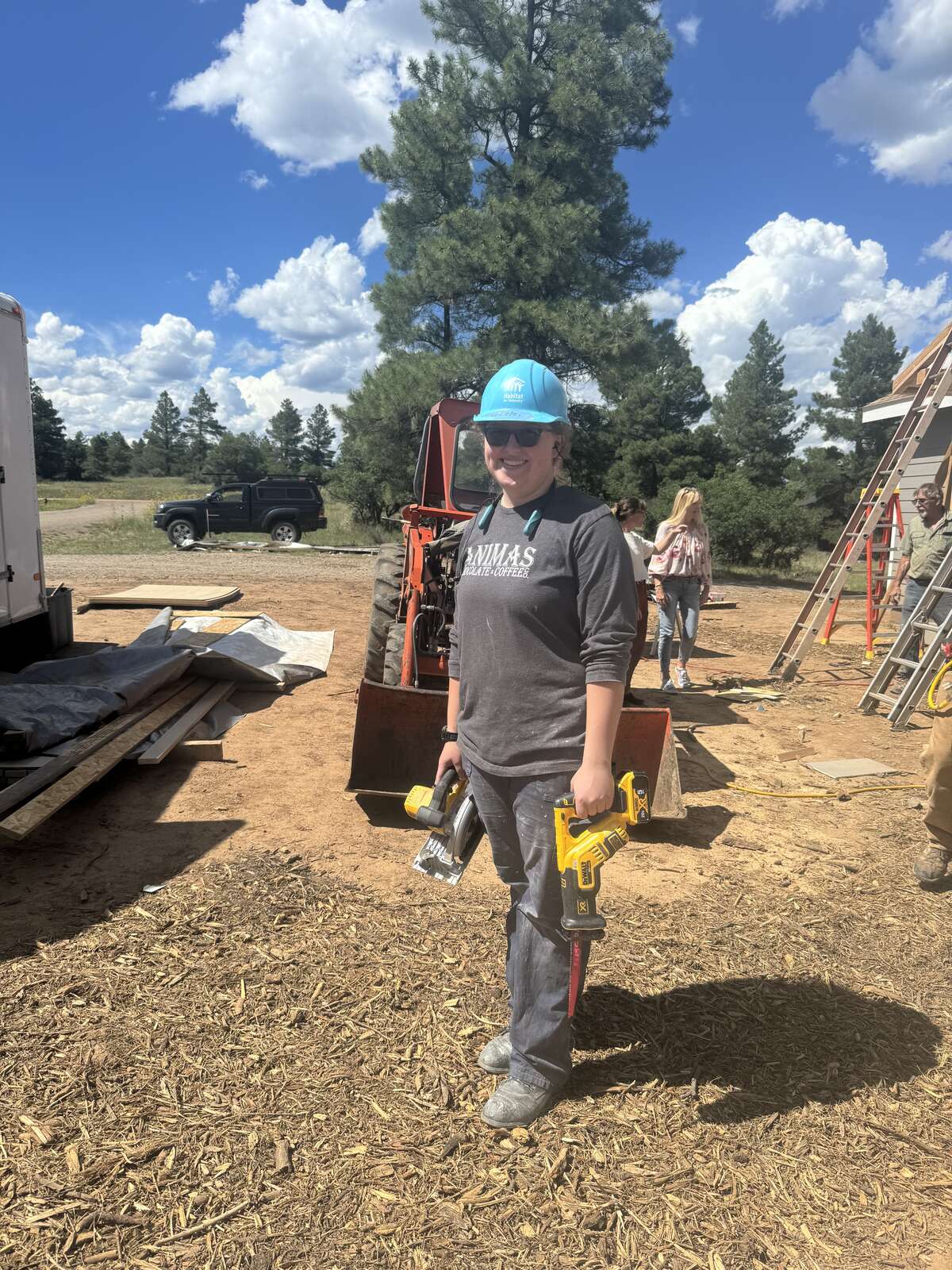 An intern in a hard hat carrying tools on an outdoor construction site