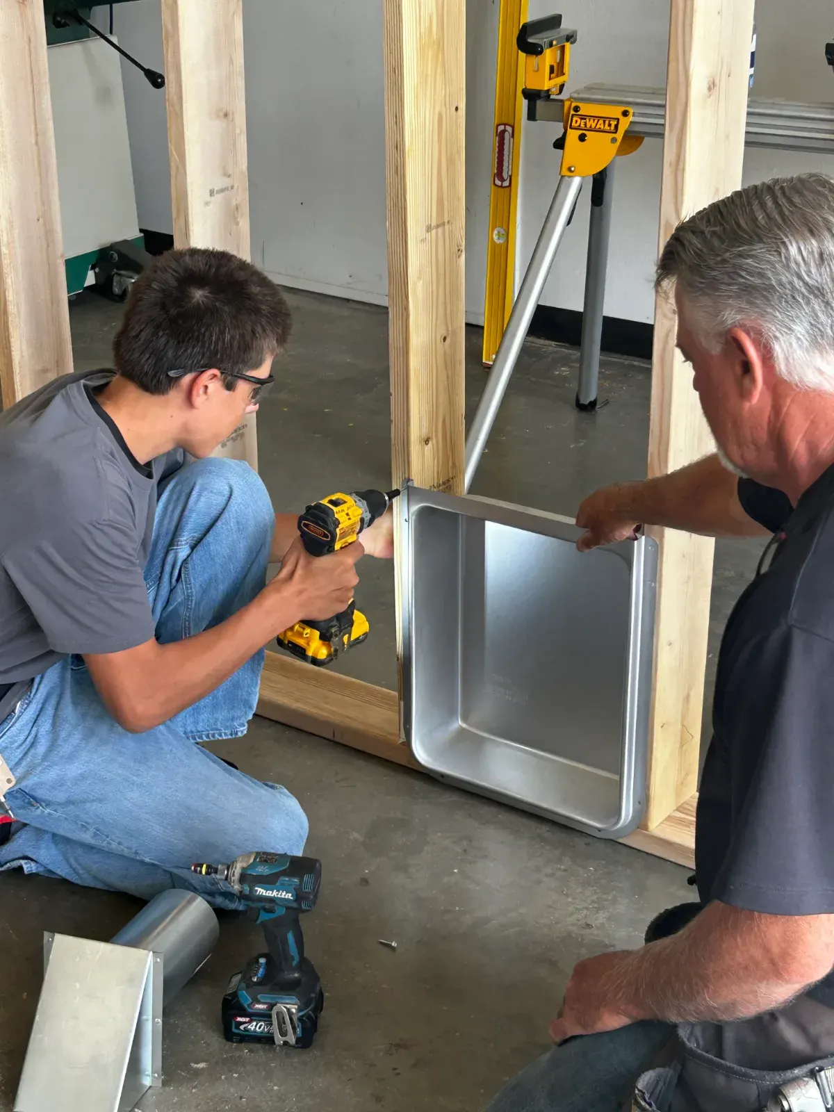 A student fitting a shower surround with a cordless drill alongside an instructor