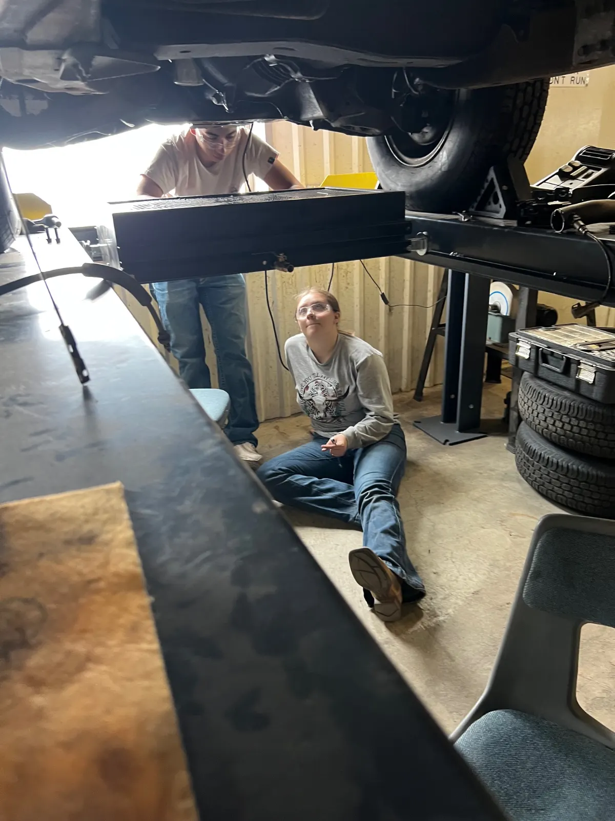 A student working beneath a vehicle on a lift in the automotive shop