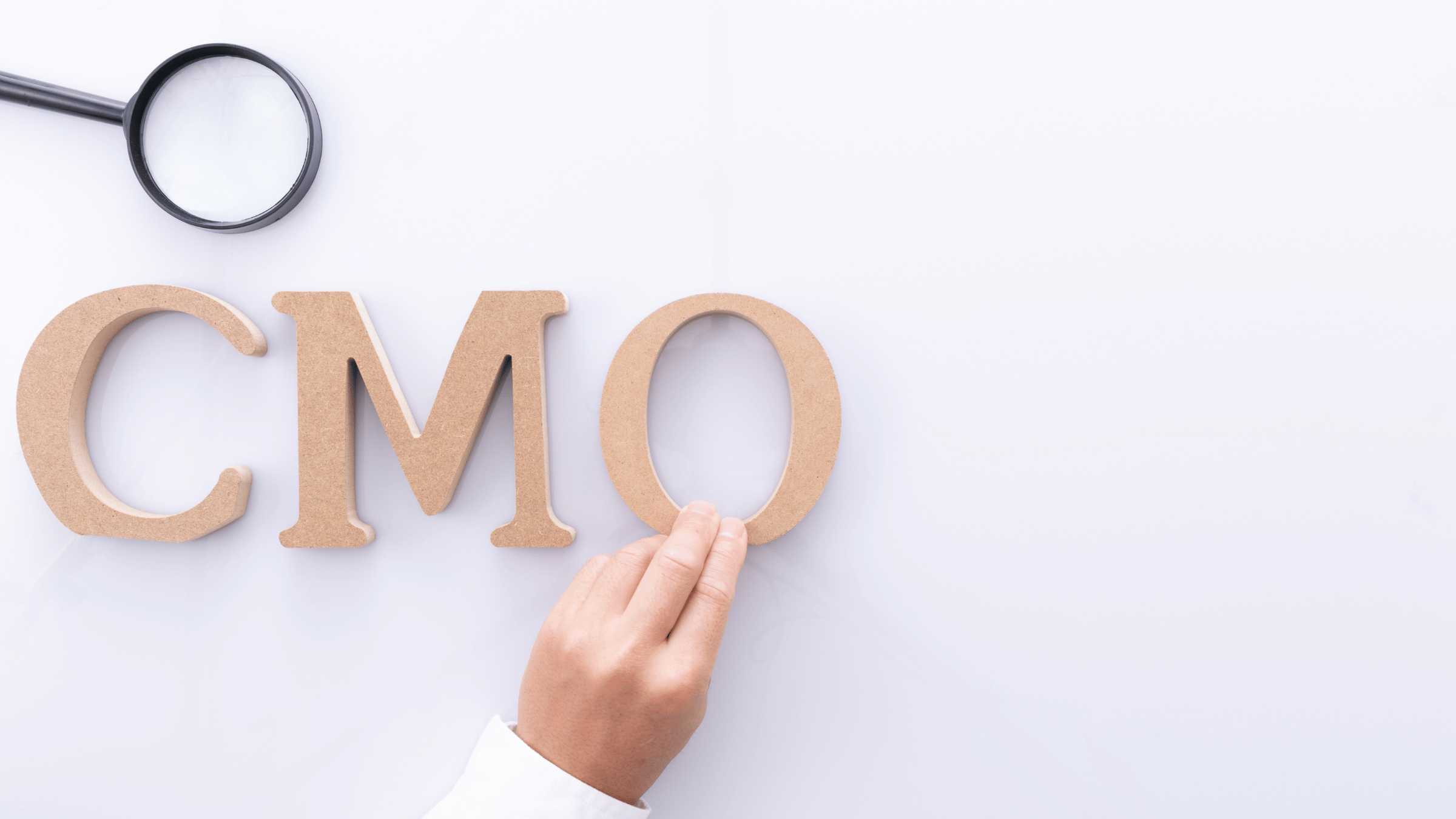 The word "CMO" spelled in wooden letters, with a hand and magnifying glass