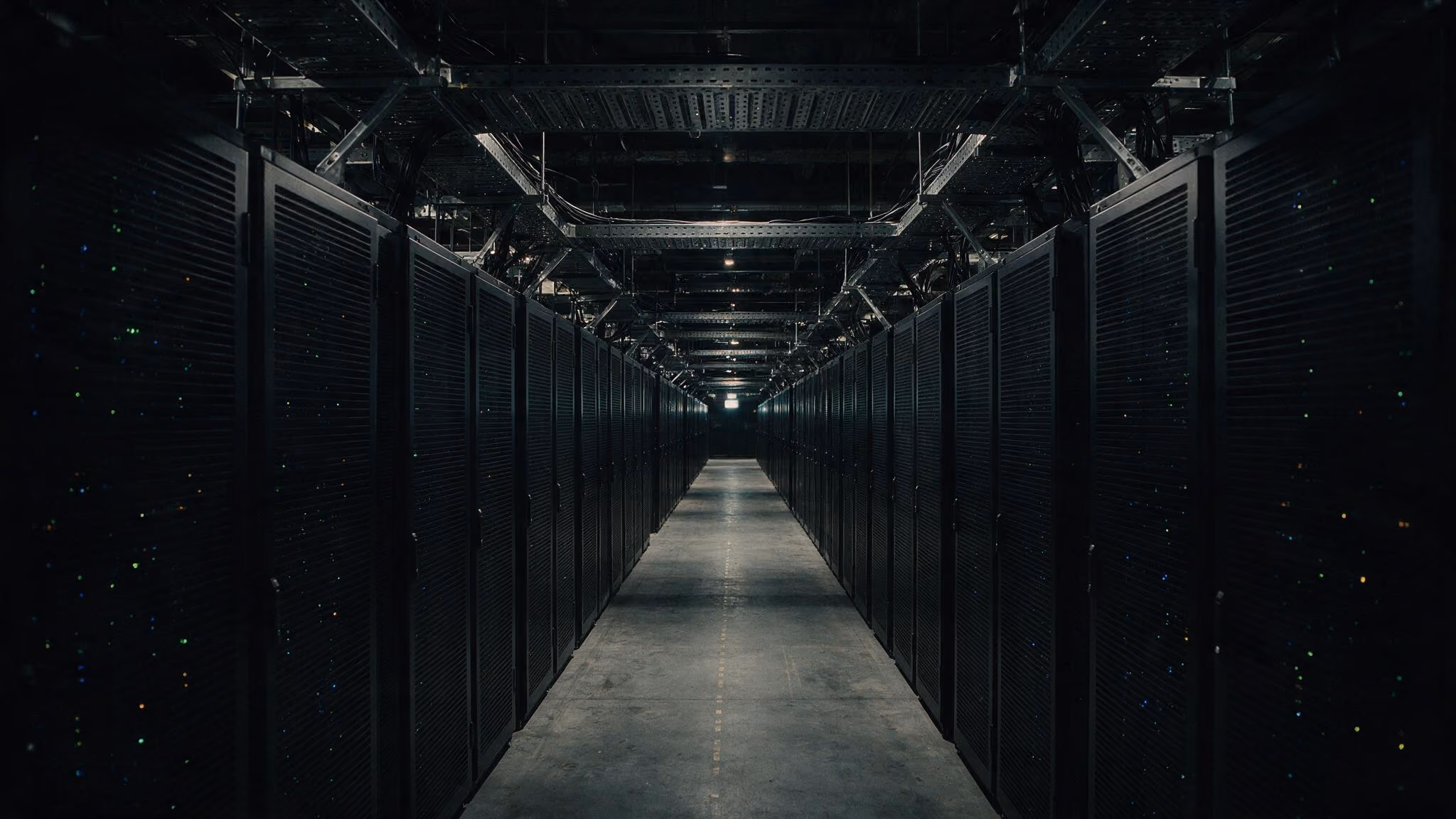 Long corridor between rows of dark server racks in a dimly lit data center.