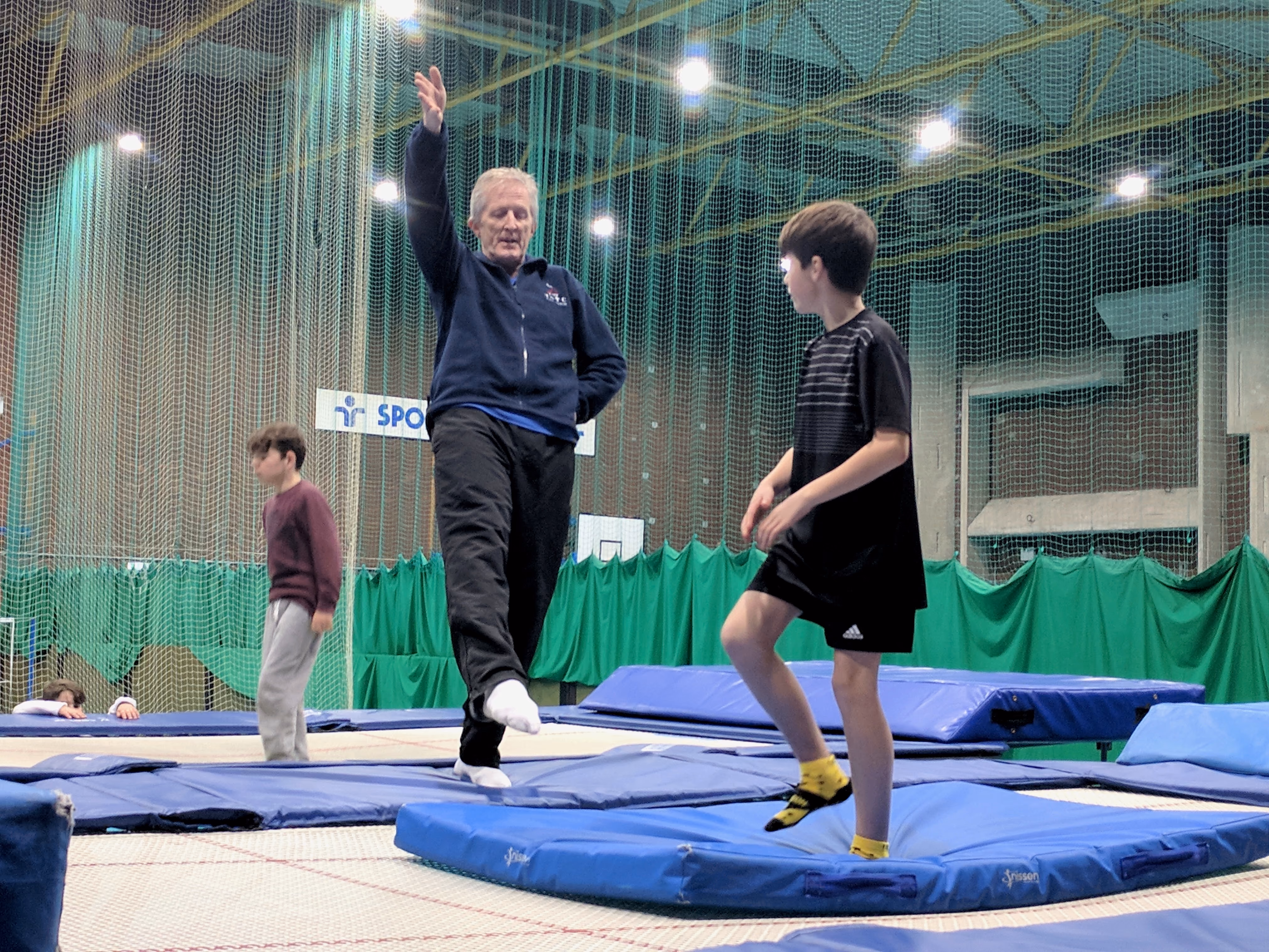 A child mid-bounce on a trampoline at Northgate Arena while a coach spots