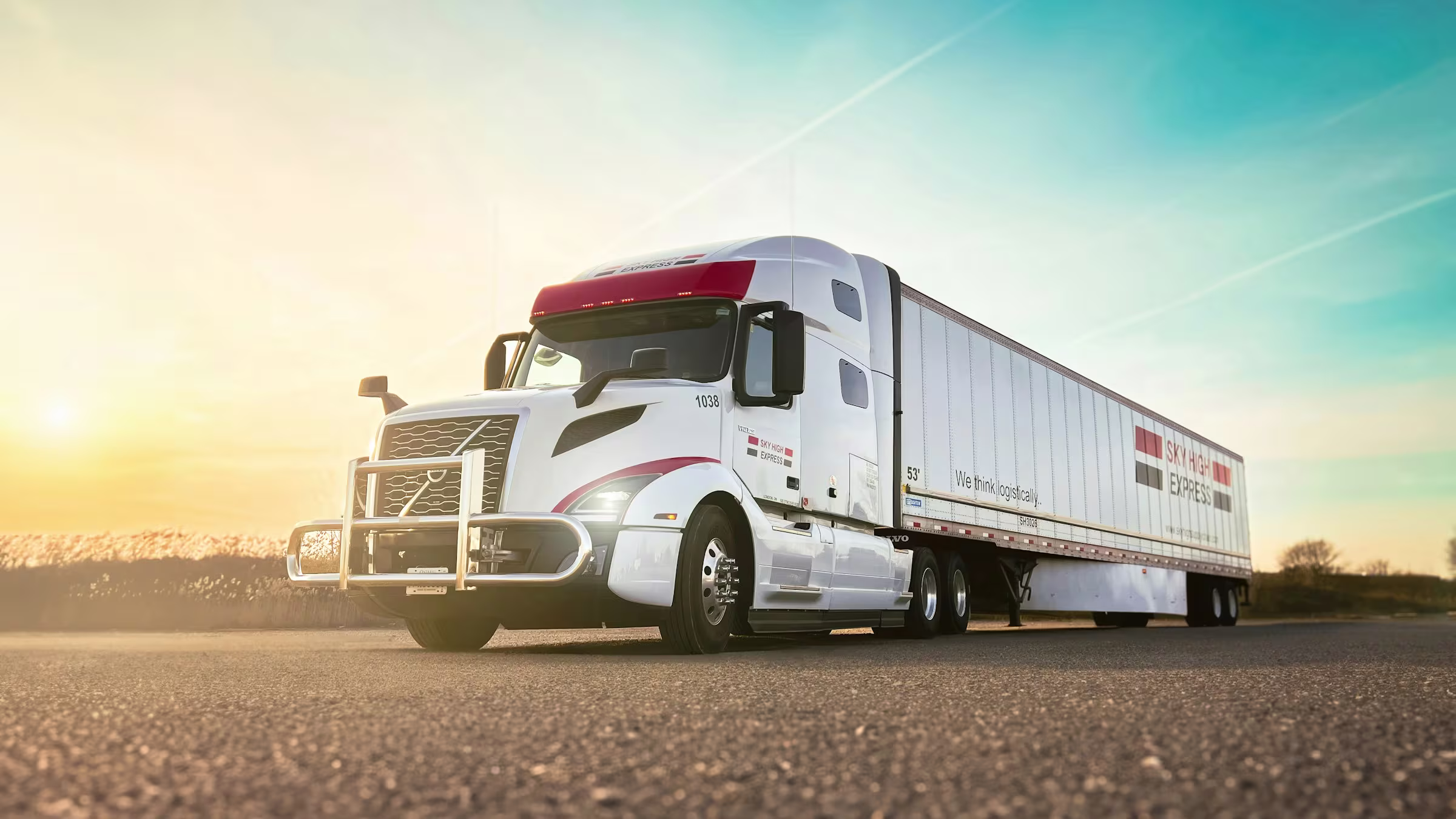 White semi truck with red accents and a large trailer parked on a road at sunset under a clear sky.